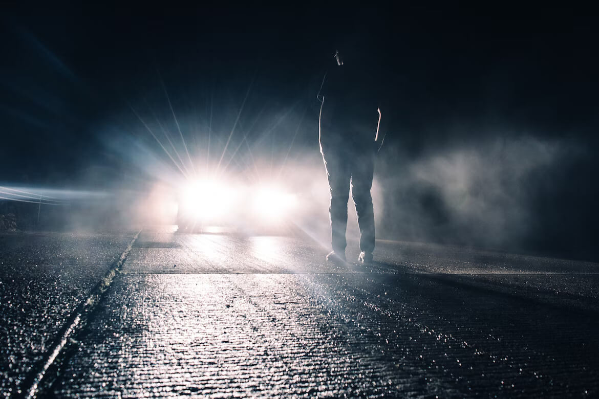 A person standing in front of the lights of a car