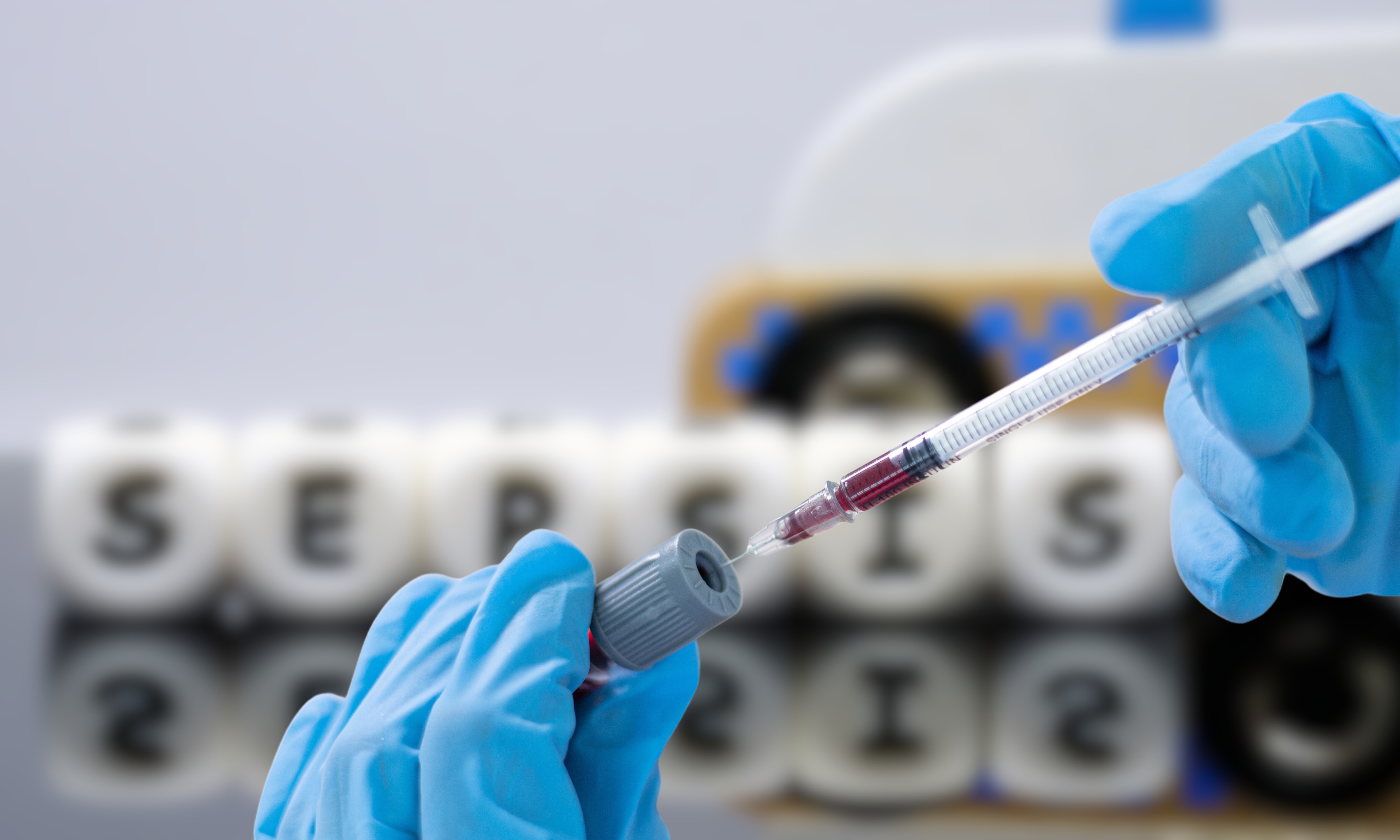 Gloved hands holding a syringe and blood vial with dice spelling SEPSIS, representing sepsis diagnosis and medical testing